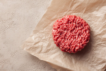 Raw ground beef meat shaped in a circle for burger patty, on wax paper. Kitchen counter background,
