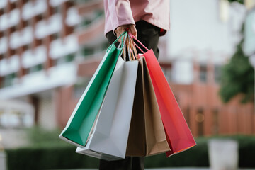 Happy young Asian woman shopping in a modern city during the evening, carrying bags, smiling,...