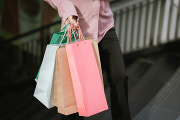 Happy young Asian woman shopping in a modern city during the evening, carrying bags, smiling, enjoying fashion, lifestyle, and urban retail experience on vacation.