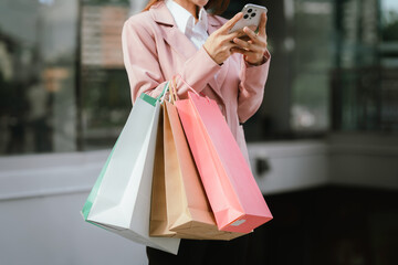 Happy young Asian woman shopping in a modern city during the evening, carrying bags, smiling,...