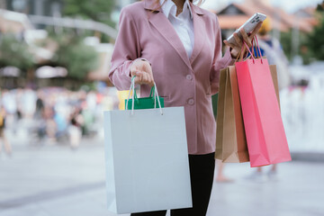 Happy young Asian woman shopping in a modern city during the evening, carrying bags, smiling,...