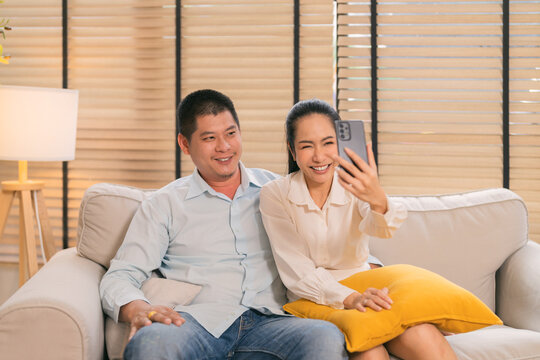 happy Asian senior couple enjoys a joyful video call with their distant family, sharing love and connection across generations. Beside them, a smiling young couple captures a cheerful selfie together 