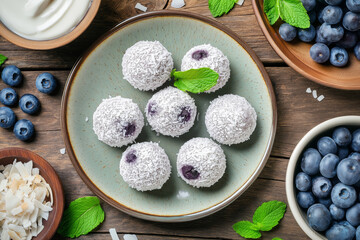 Frozen Blueberry and Coconut Yogurt Bites made of smooth unsweetened coconut yogurt and fresh blueberries, garnished with shredded coconut and fresh mint, arranged on a ceramic plate.