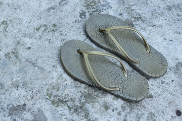 Photo of a pair of flip-flops with worn gray soles and cracks on the soles of the feet and gold...