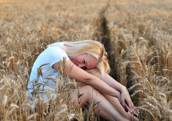 Woman with long hair in pink dress stands in golden wheat field during sunset, highlighting natural...