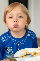 A child wearing a blue shirt is sitting at a table and eating enthusiastically. The moment captures a sense of appetite and the carefree nature of childhood. Diet for kids, homemade food