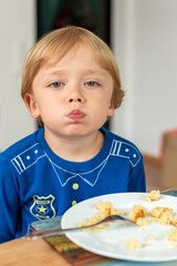 A child wearing a blue shirt is sitting at a table and eating enthusiastically. The moment captures a sense of appetite and the carefree nature of childhood. Diet for kids, homemade food