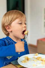A child wearing a blue shirt is sitting at a table and eating enthusiastically. The moment captures a sense of appetite and the carefree nature of childhood. Diet for kids, homemade food