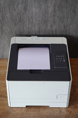 This front-facing shot of printer with a single sheet of paper outing from its top output tray.