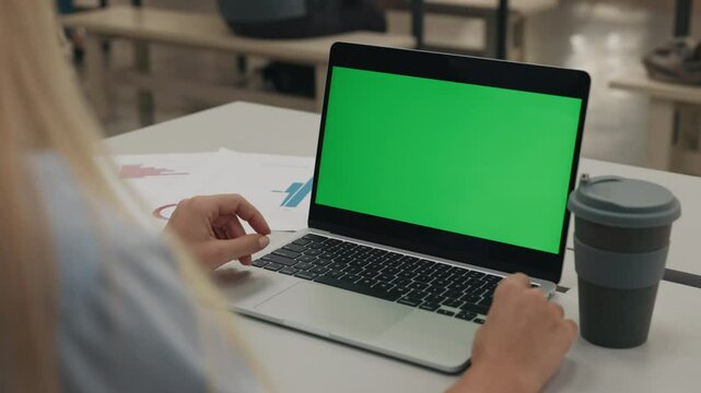 Businesswoman sits at laptop with chroma key screen at office desk closeup. Corporate employee works on computer with coffee cup standing at workplace. Advertising mockup device