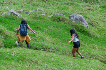 Two female tourists hiking down a lush green hill
