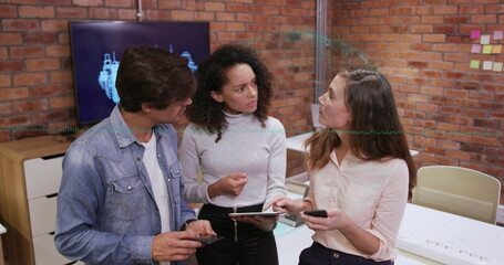 Three coworkers discussing blueprint on monitor in exposed brick workspace, using tablet smartphone © vectorfusionart