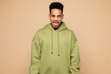 Young sad mad angry indignant outraged man of African American ethnicity in green hoodie casual clothes scream shout isolated on plain pastel light beige background studio portrait Lifestyle concept