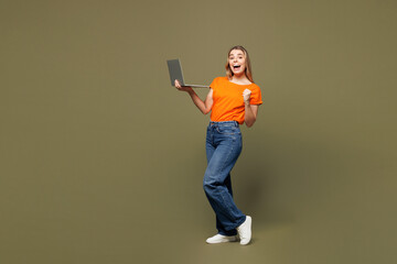 Full body young smiling IT woman wears orange t-shirt casual clothes hold use work on laptop pc computer do winner gesture isolated on plain pastel green background studio portrait. Lifestyle concept.