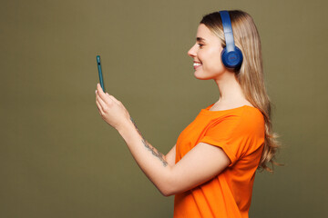 Side view young smiling woman she wears orange t-shirt casual clothes listen to music in headphones...