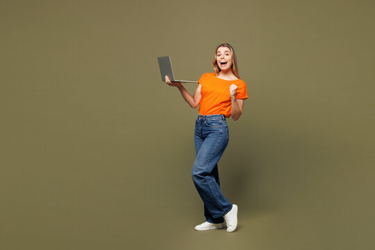 Full body young smiling IT woman wears orange t-shirt casual clothes hold use work on laptop pc computer do winner gesture isolated on plain pastel green background studio portrait. Lifestyle concept. - Powered by Adobe
