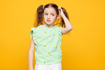 Little minded pensive thoughtful kid child girl 8-9 years old wear green t-shirt put hand on head scratch it look aside isolated on plain yellow background. Mother's Day love family lifestyle concept