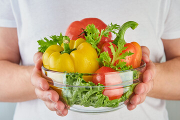 Man in white T shirt hands holding pepper, tomato, lettuce in glass plate. Healthy lifestyle, nutrition and dieting concept background. Element for design.