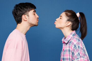Side profile view young couple two friends family man woman they wearing pink casual clothes together going to kiss each other isolated on plain blue wall background studio portrait Lifestyle concept