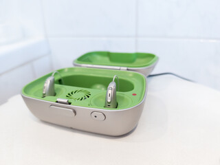 pair of modern rechargeable hearing aids placed in a green and gray charging case. Hearing devices designed for individuals with hearing loss, medical technology and senior healthcare solutions, every