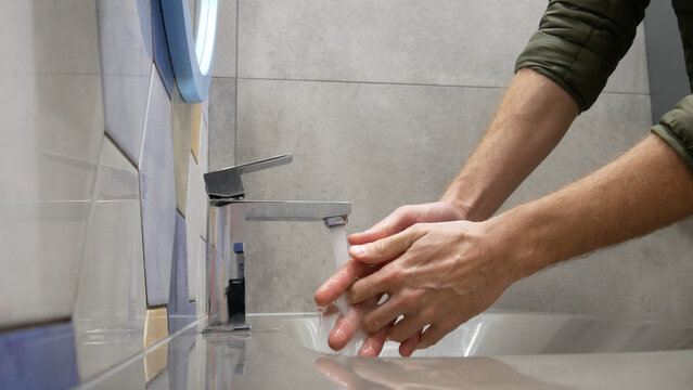 Close-up of a restroom faucet and a man washing the hands