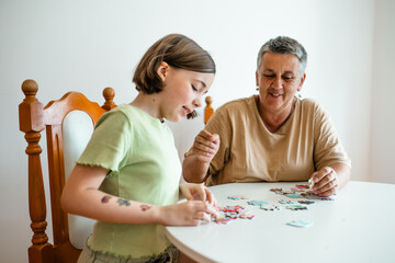 Grandmother and granddaughter doing puzzle at home.