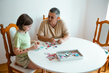 Grandmother and granddaughter doing puzzle at home.