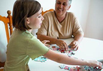 Grandmother and granddaughter doing puzzle at home.
