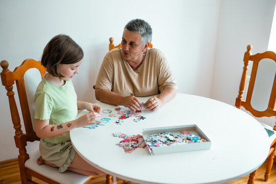 Grandmother and granddaughter doing puzzle at home. - Powered by Adobe
