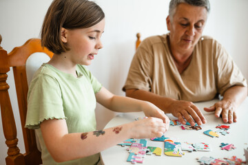 Fototapeta premium Grandmother and granddaughter doing puzzle at home.