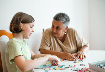 Grandmother and granddaughter doing puzzle at home.