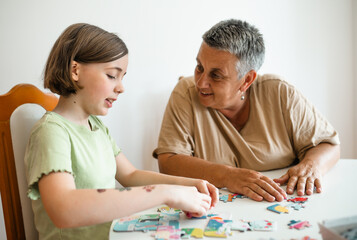 Grandmother and granddaughter doing puzzle at home.