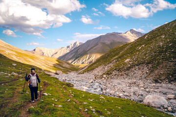 Fototapeta premium Photo from the back of a hiker walking on green grasslands in the Tianshan Mountains in Xinjiang, China. There is snow on the peak with copy space on top. The idea for adventure activity wallpaper.