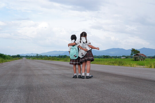 Rear view of energetic elementary middle school kids with backpack in School uniform,Children walk on the street have fun, jump, dance, sing, Concept of Back to school and The bond of friends forever.