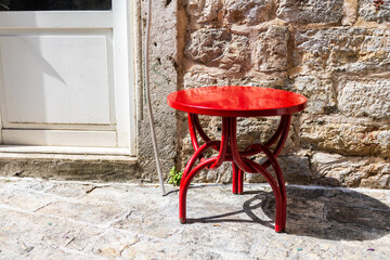 Bright red stool beside stone wall. Street furniture, color contrast, and outdoor simplicity.