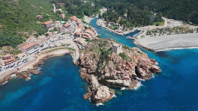 Aerial view above the Genoise tower on a rocky outcrop, the beach and town of Porto on the west coast of the Mediterranean island of Corsica with mountains behind
