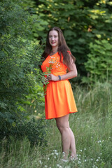 Portrait of a young beautiful girl in an orange dress in a summer forest.