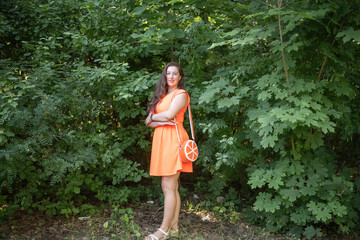 Portrait of a young beautiful girl in an orange dress in a summer forest.