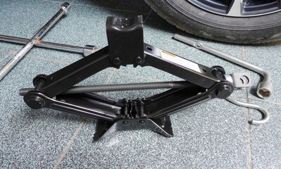 Jack, wheel wrench next to car wheel in garage. DIY illustration on vehicle.