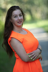 Portrait of a young beautiful girl in an orange dress in a summer forest.