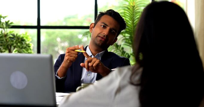 Indian businessman interviewing female candidate sitting across table, Asian corporate man woman in professional attire meeting in modern office with laptop, documents, woman seen from back sitting