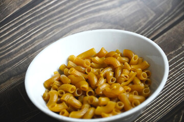 fresh raw elbow macaroni served in a bowl on wooden background