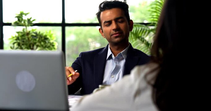Indian businessman interviewing female candidate sitting across table, Asian corporate man woman in professional attire meeting in modern office with laptop, documents, woman seen from back sitting