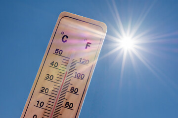 Fototapeta na wymiar Thermomètre affichant une température élevée en degrés Celsius et Fahrenheit avec un soleil rayonnant sur fond de ciel bleu. Concepts d'été, de beau temps, de chaleur excessive et de canicule 