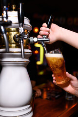 A close-up shot of the moment beer is poured from a stylish bar tap, with the foam slowly rising in a tilted glass held in both hands.