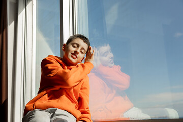 Young boy in orange hoodie gazing out window