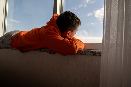 Young boy gazing out window in orange hoodie