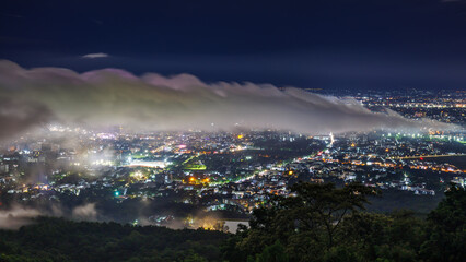 Aerial view of city skyline landscape at night with misty clouds over the illuminated cityscape...