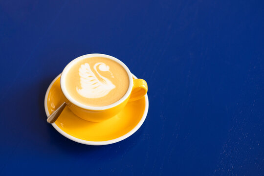 Swan latte art in yellow cup on blue background