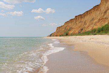 A scenic view of a vast sandy beach bordered by majestic towering cliffs, with gentle waves rolling into the shore under a clear sky with scattered clouds.
